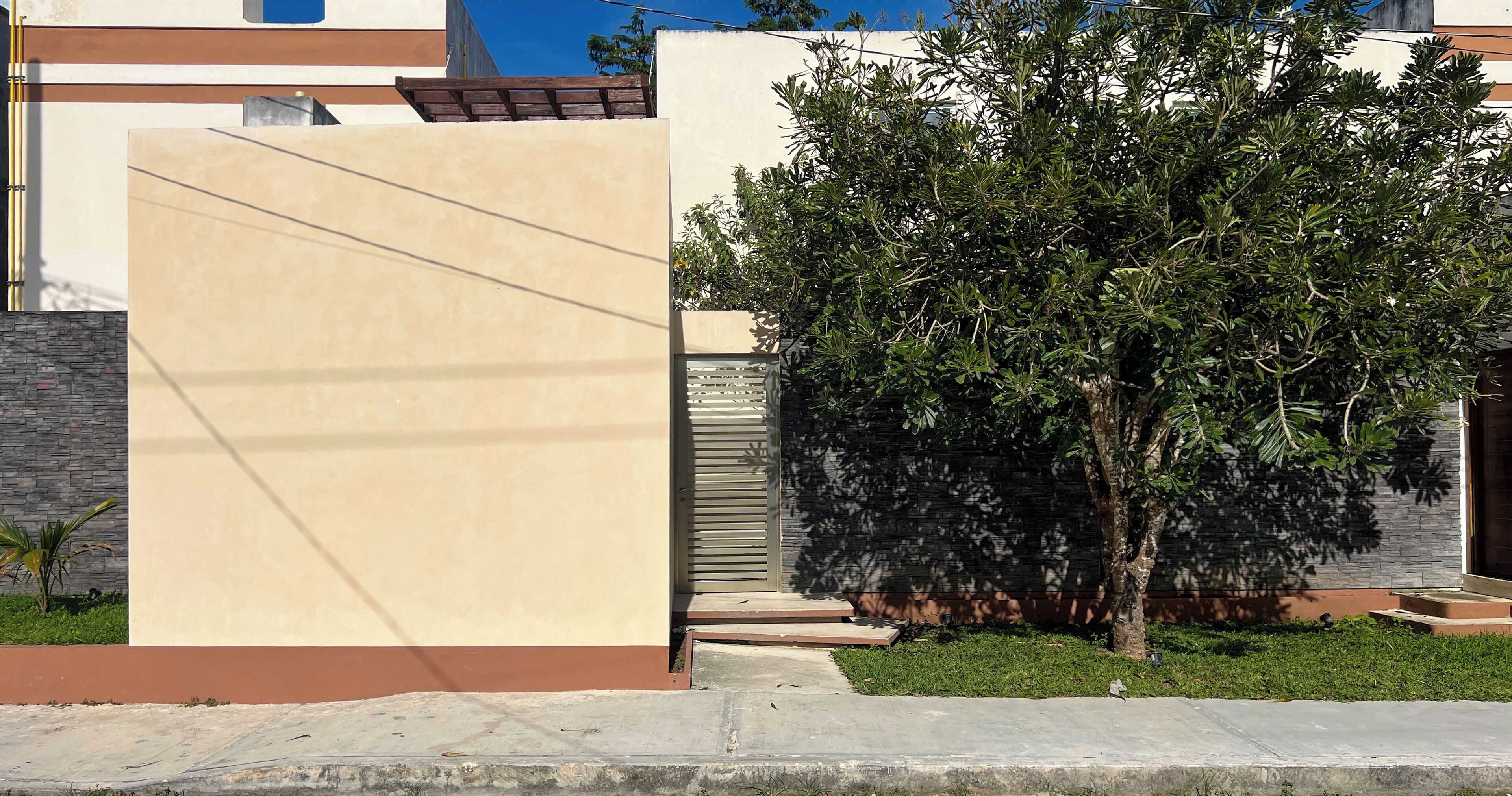 A modern building with a beige facade, a tree in front, and a metal gate.