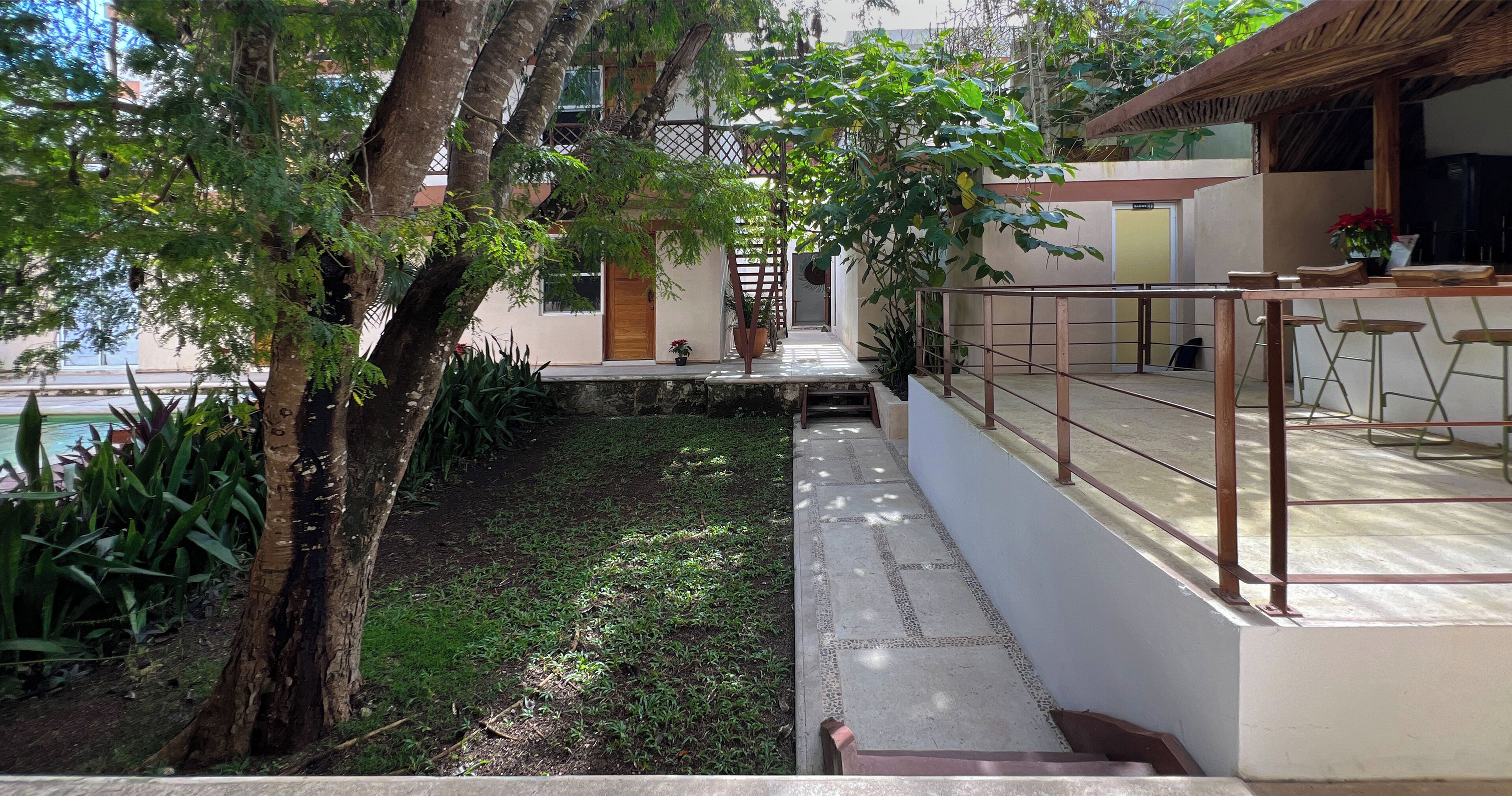 Un patio con una estructura de techo de paja, un área de descanso con sillas y vista a un edificio con puerta de madera.