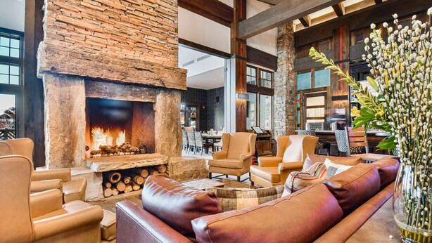A cozy interior with a stone fireplace, leather seating, and a dining area. - Powder Peak by Avantstay Ski In And Out (Park City)