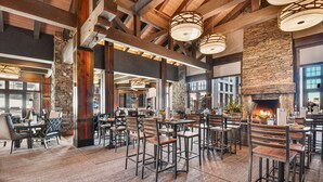 A spacious restaurant with high ceilings, exposed beams, and a stone fireplace. Tables and chairs are arranged for dining. - Powder Peak by Avantstay Ski In And Out (Park City)