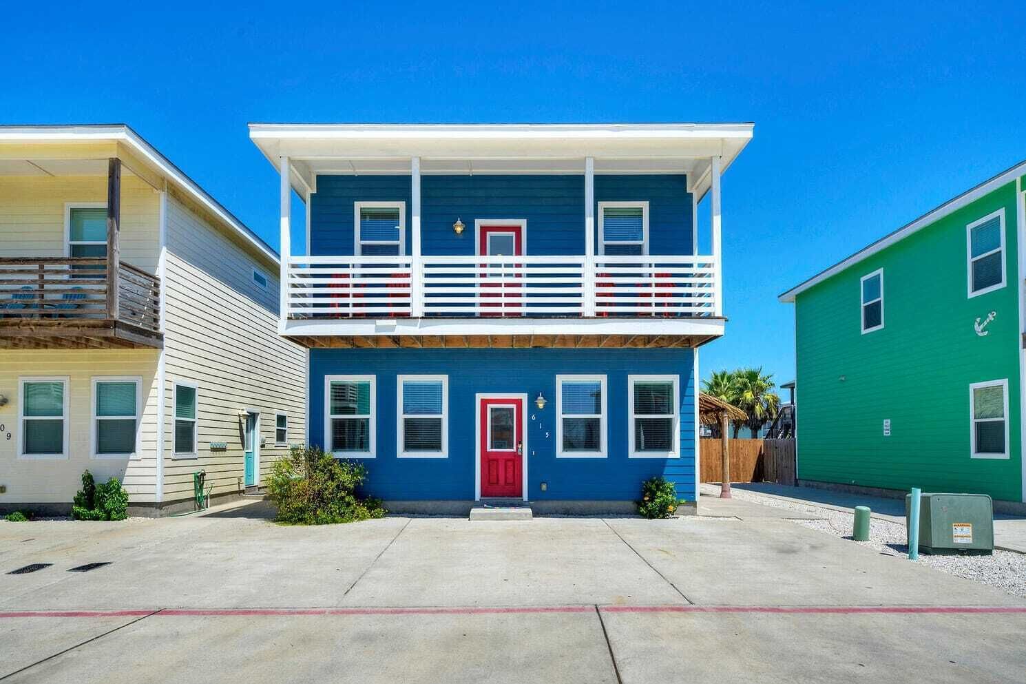 A two-story building with a red door and white-framed windows, located in a residential area with a clear blue sky.