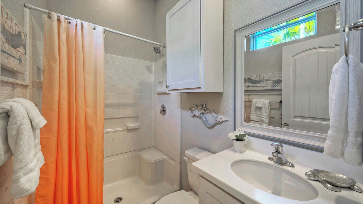 A bathroom with a shower, toilet, sink, and a mirror.