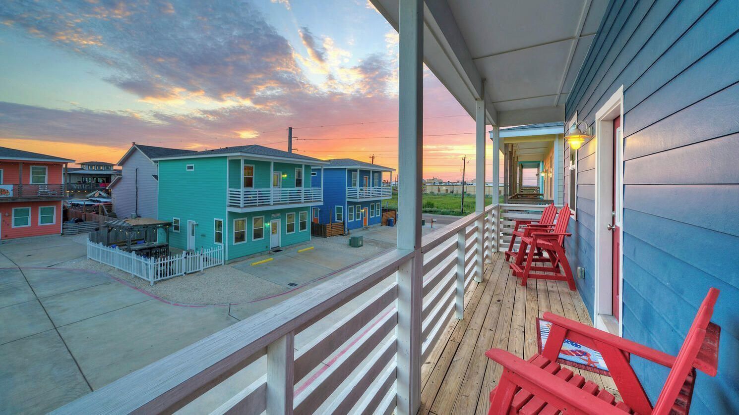 A motel with a porch, red chairs, and a view of other buildings.