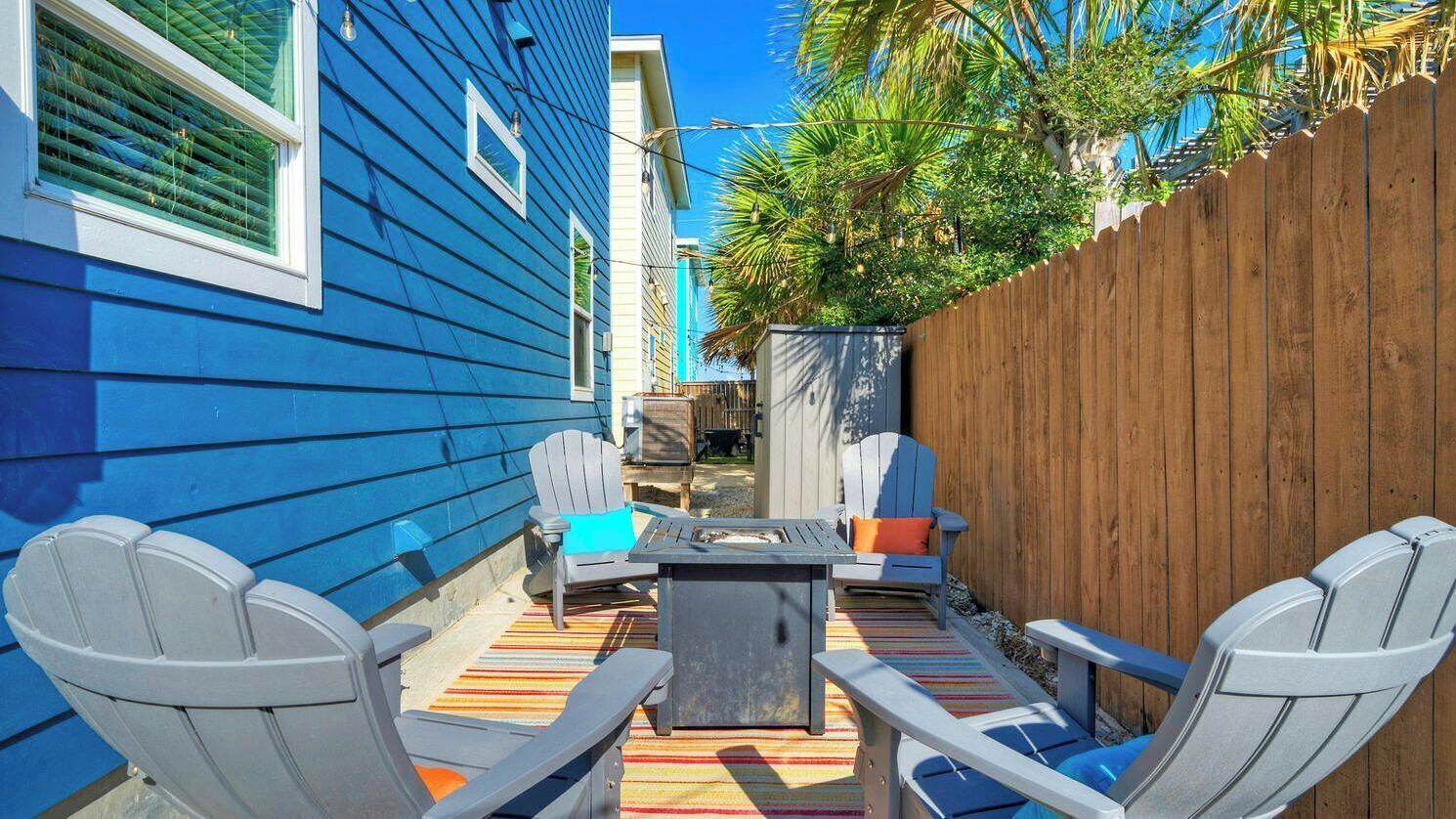 A patio with Adirondack chairs, a table, and a wooden fence.