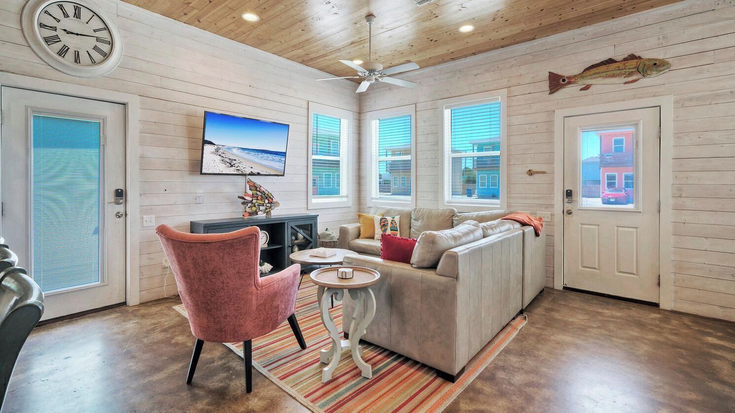 A cozy living room with a sofa, a chair, a TV, and a fish decoration on the wall.