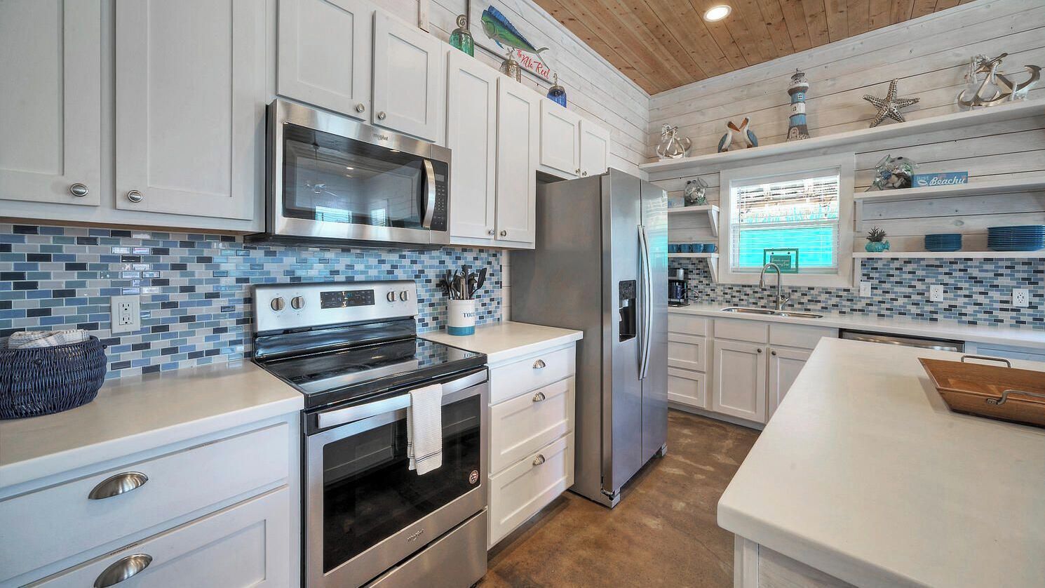 Una cocina moderna con armarios blancos, un refrigerador de acero inoxidable y un salpicadero de azulejos azules.