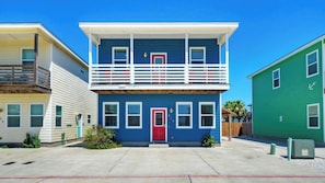 Un immeuble résidentiel de deux étages avec une porte rouge, des balustrades blanches et un balcon.