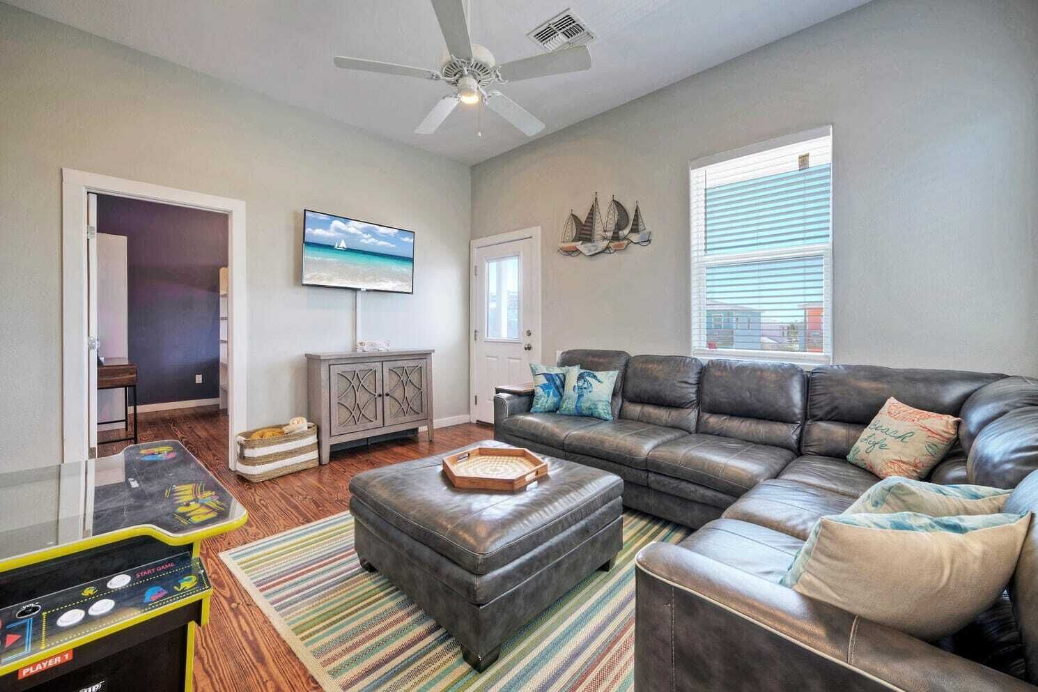 A living room with a leather sofa, a television, a ceiling fan, and a striped rug.