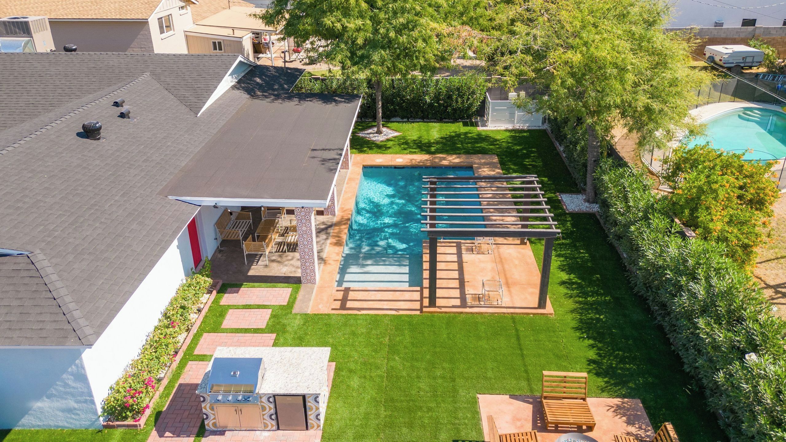 Un jardin à l’arrière d’une maison, avec une piscine, du mobilier de jardin et un espace barbecue.