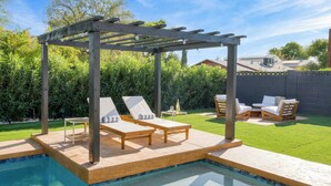 Ein Poolbereich mit Pergola, Liegestühlen und einem Tisch mit Flasche und Glas.