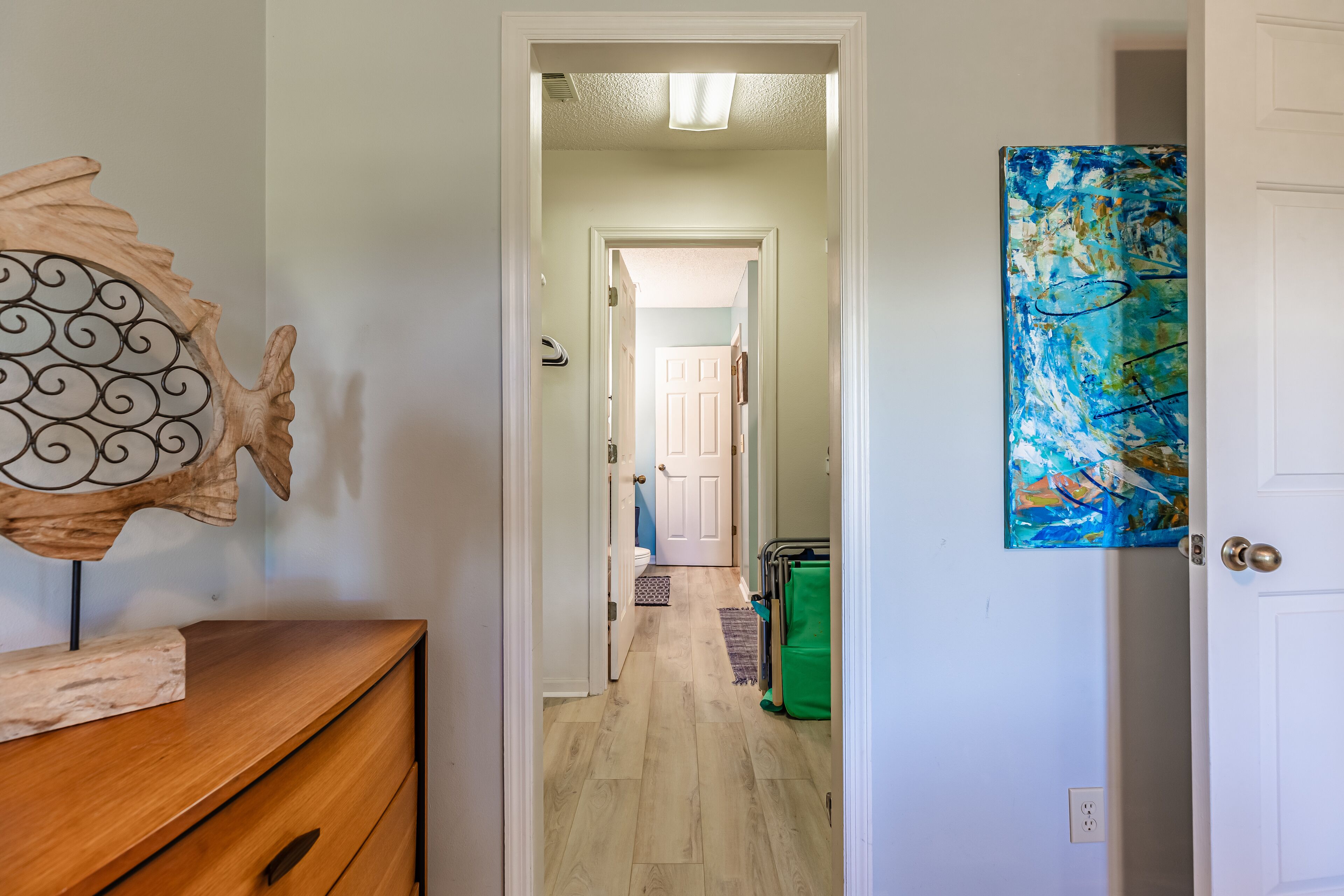 A hallway with a wooden dresser, a decorative wall piece, and a door with a blue abstract painting.