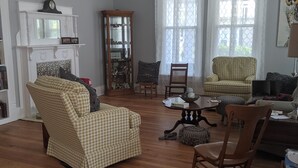 A spacious living room with hardwood flooring, a chandelier, a fireplace, and a large window with sheer curtains. - M G Richardson Bed & Breakfast (Richland)