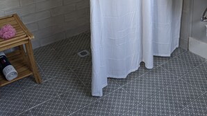 A bathroom with a white shower curtain, a wooden stool with a pink object, and a sink with a bottle of liquid soap. - M G Richardson Bed & Breakfast (Richland)