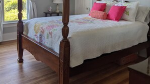 A four-poster bed with a floral quilt, a bedside table with a lamp, and a framed floral picture on the wall. - M G Richardson Bed & Breakfast (Richland)