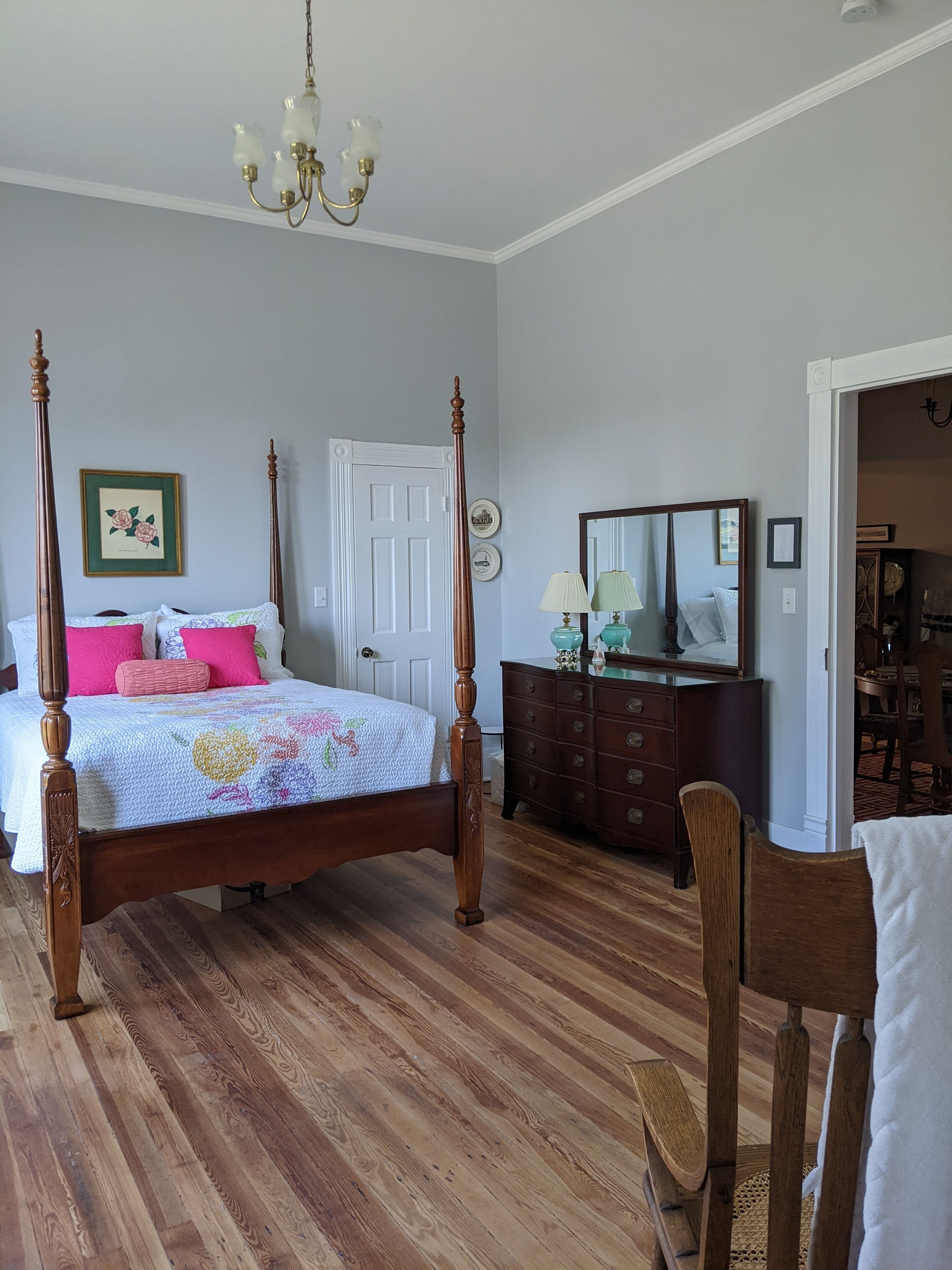 Un lit à baldaquin avec une couvre-lit à motifs floraux, une commode en bois et un miroir.