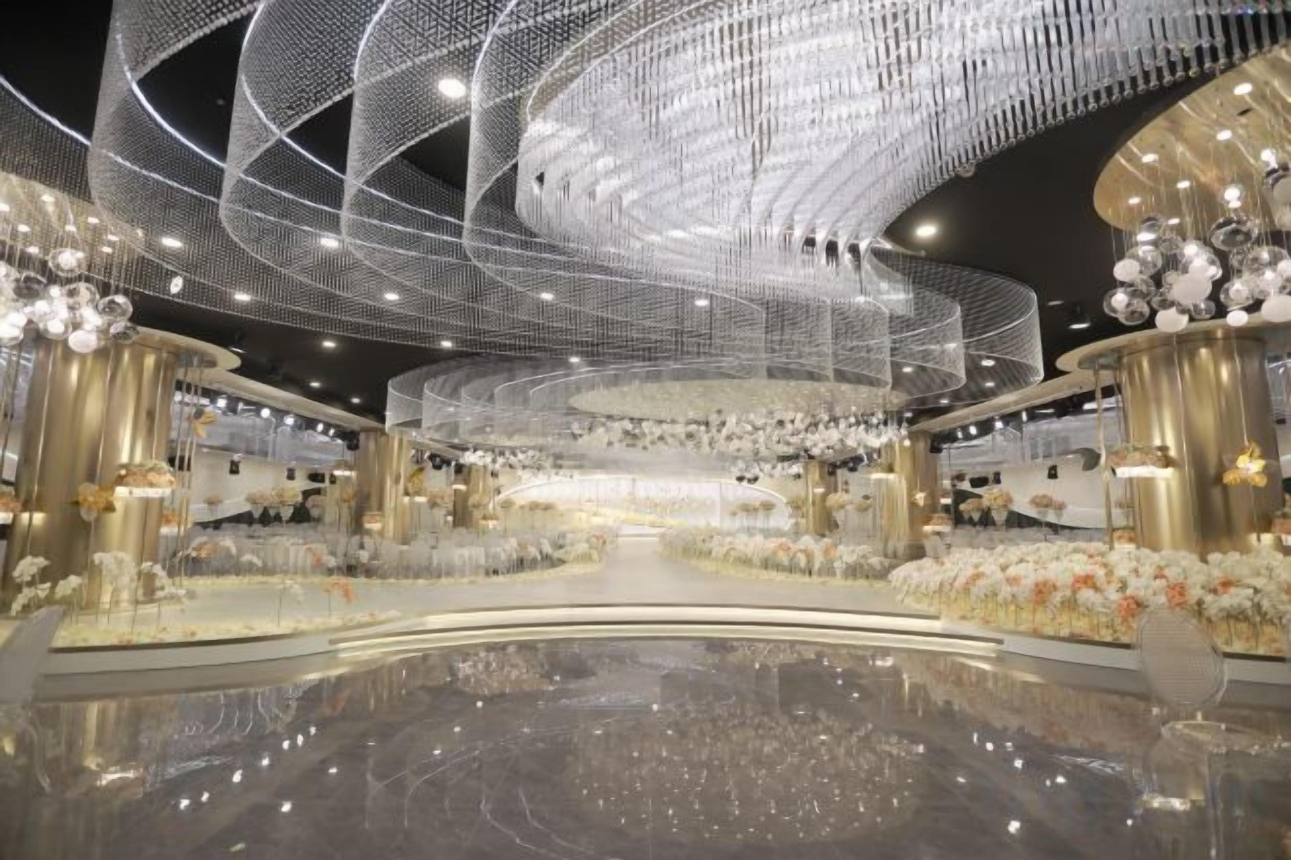 A spacious indoor venue with a reflective floor, a central stage, and a ceiling adorned with intricate light fixtures.