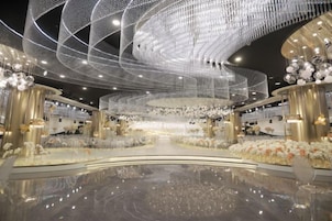 Un espacio interior amplio con piso reflectante, un escenario central y un techo decorado con elaboradas luminarias.
