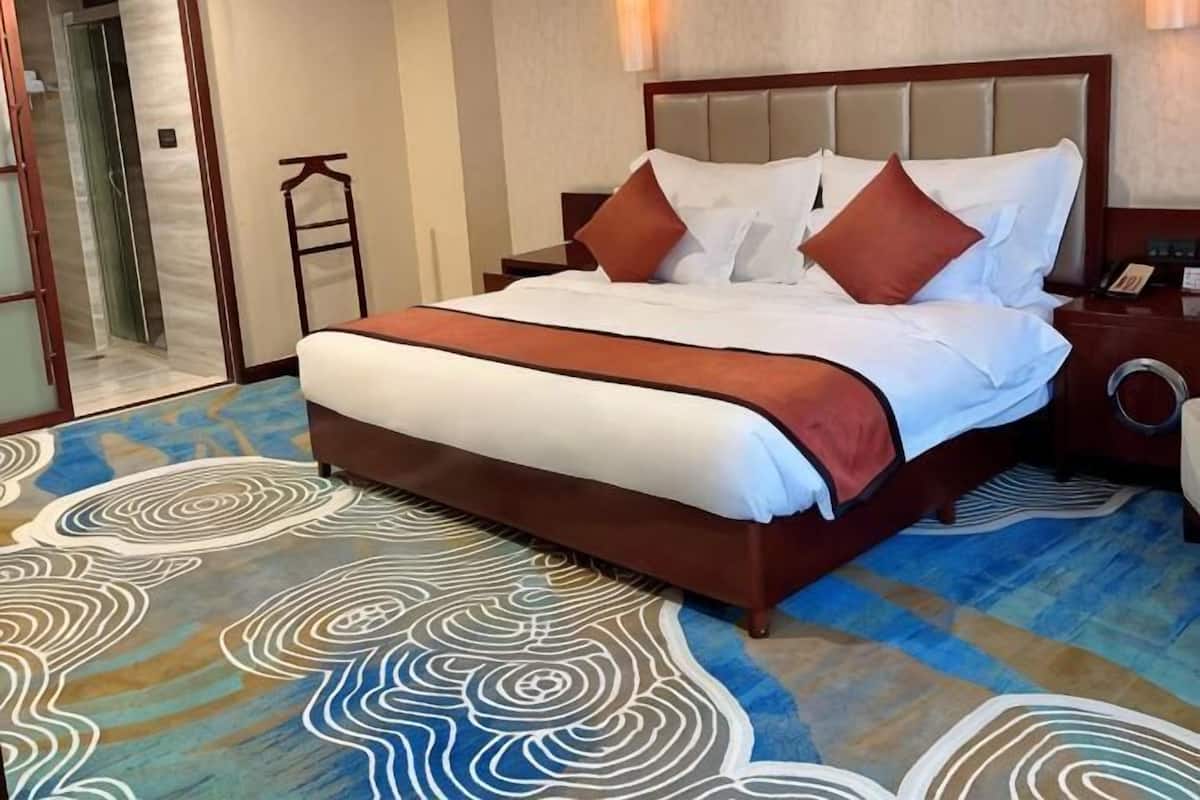 Ein Hotelzimmer mit einem großen Bett, einem Nachttisch, einer Lampe und einem gemusterten Teppich.