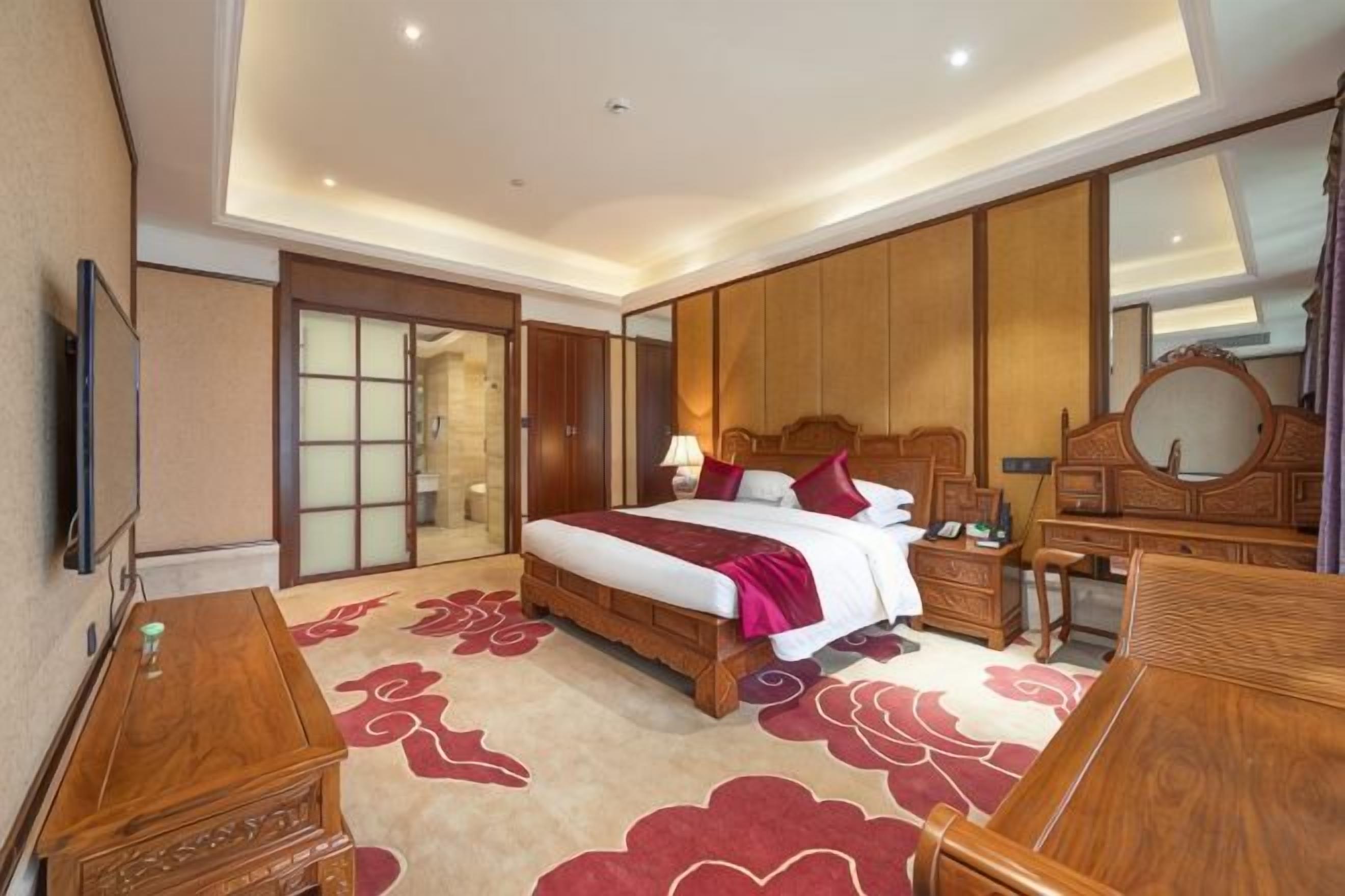A hotel room with a large bed, a wooden dresser, a desk, and a mirror.