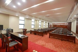 Un salón de conferencias con hileras de sillas, un atril y piso alfombrado.
