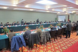 Un salón de conferencias con una larga mesa, varias sillas y asistentes sentados.