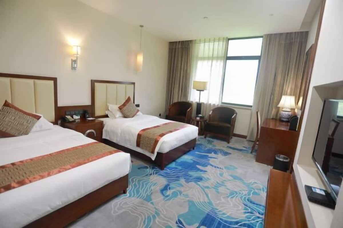 Ein Hotelzimmer mit zwei Betten, einem Fernseher, einem Schreibtisch und einem Stuhl.