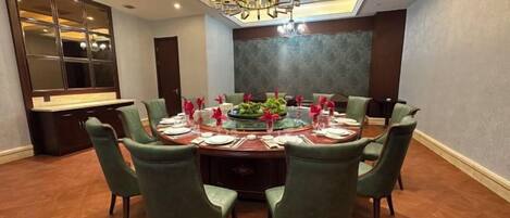 A dining room with a round table set for six, surrounded by green upholstered chairs.