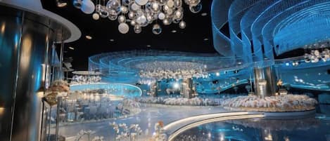 A modern interior with a central circular platform, surrounded by seating areas and a large, intricate chandelier.