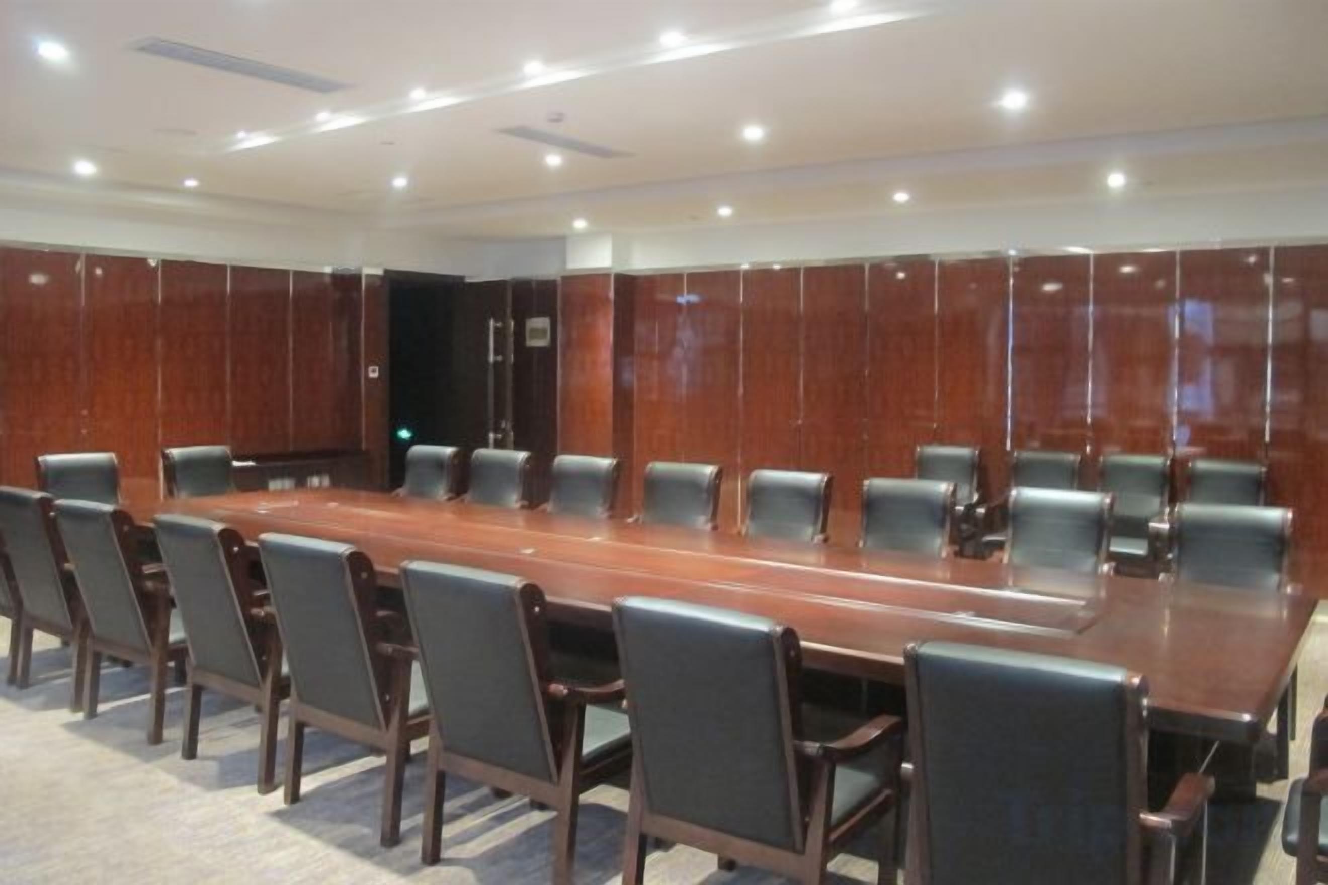 A conference room with a long table surrounded by chairs, wooden paneling on the walls, and recessed ceiling lighting.