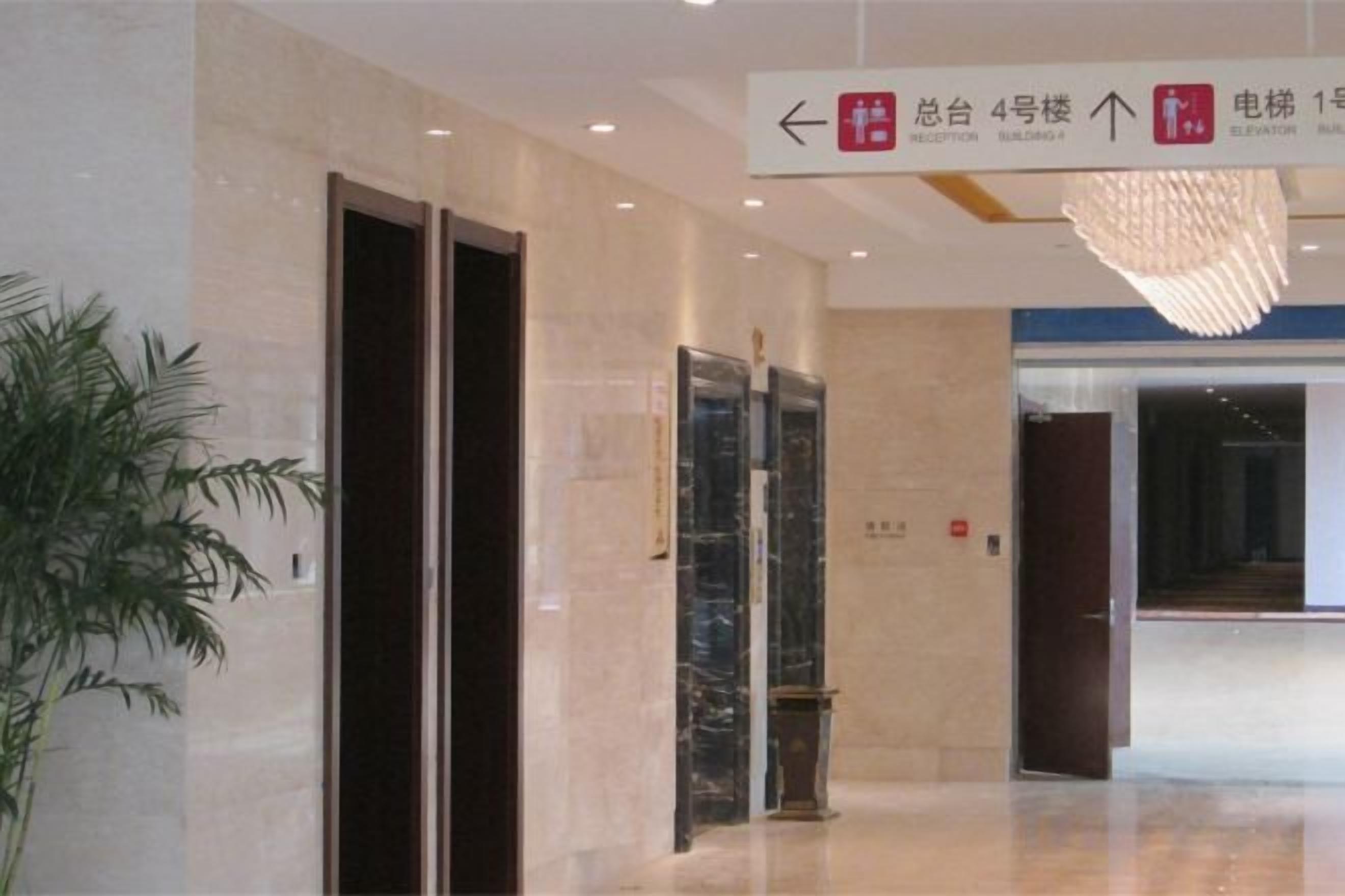 An interior corridor with a modern elevator, a directional sign, and a potted plant.