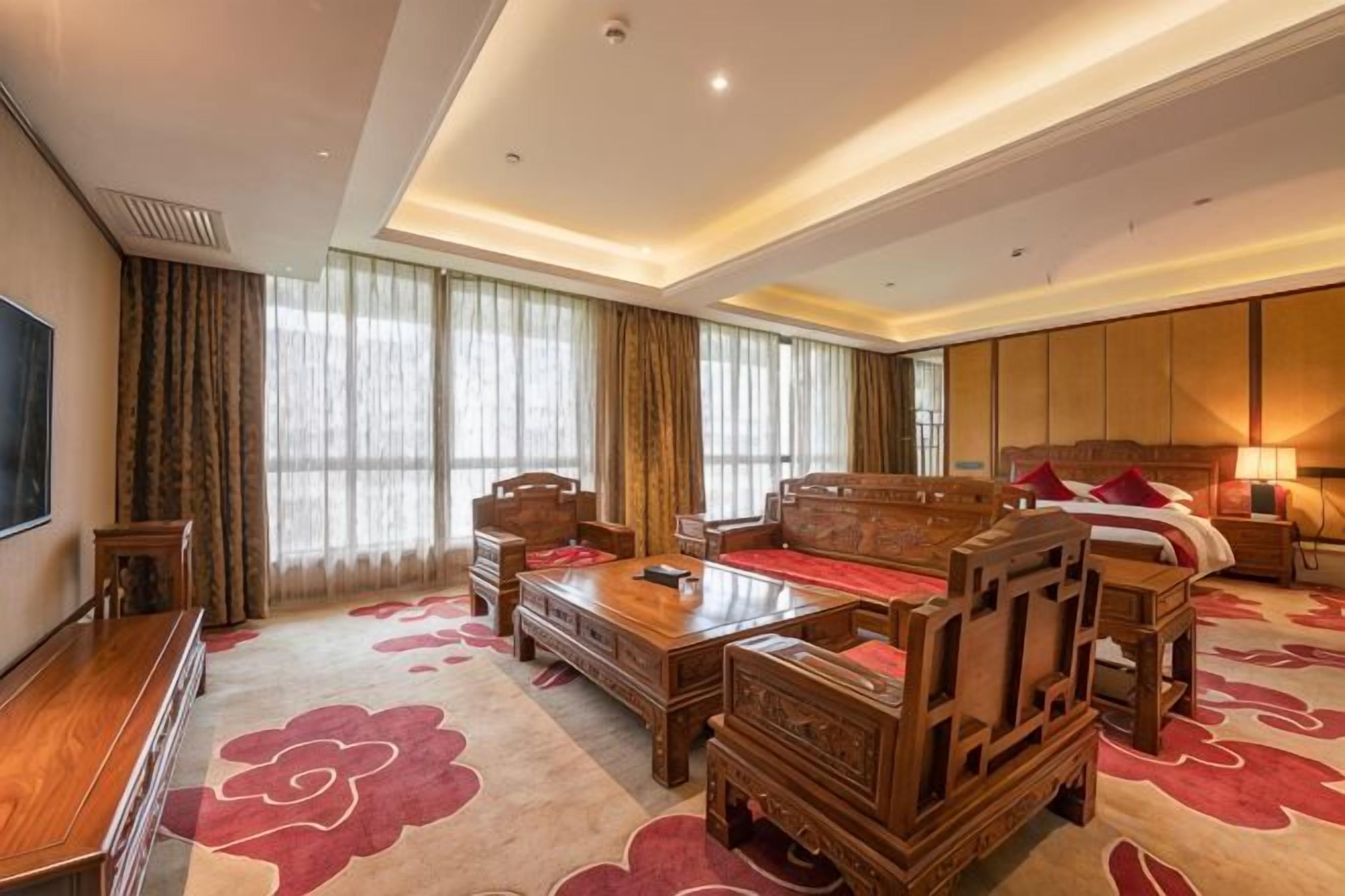 Habitación de hotel con una cama grande, un sofá de madera, una mesita de centro de madera y un televisor en la pared izquierda.