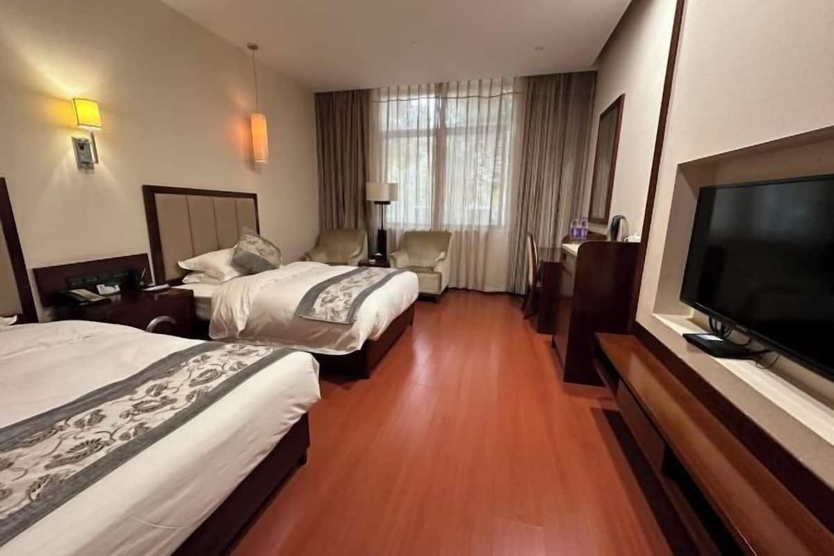 Ein Hotelzimmer mit zwei Betten, einem Fernseher, einem Schreibtisch und einem Vorhangfenster.