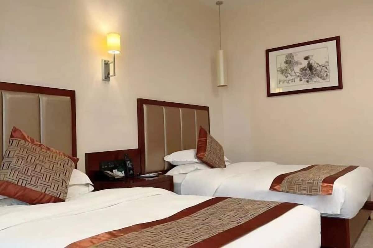 Ein Hotelzimmer mit zwei Betten, einem Nachttisch, einer Lampe und einem gerahmten Bild an der Wand.