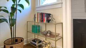 A room with a wooden floor, a bookshelf, a potted plant, a fireplace, and a window with natural light. - HOLLY HOUSE ~ Organic, Dog-friendly Garden Cottage (Medford)