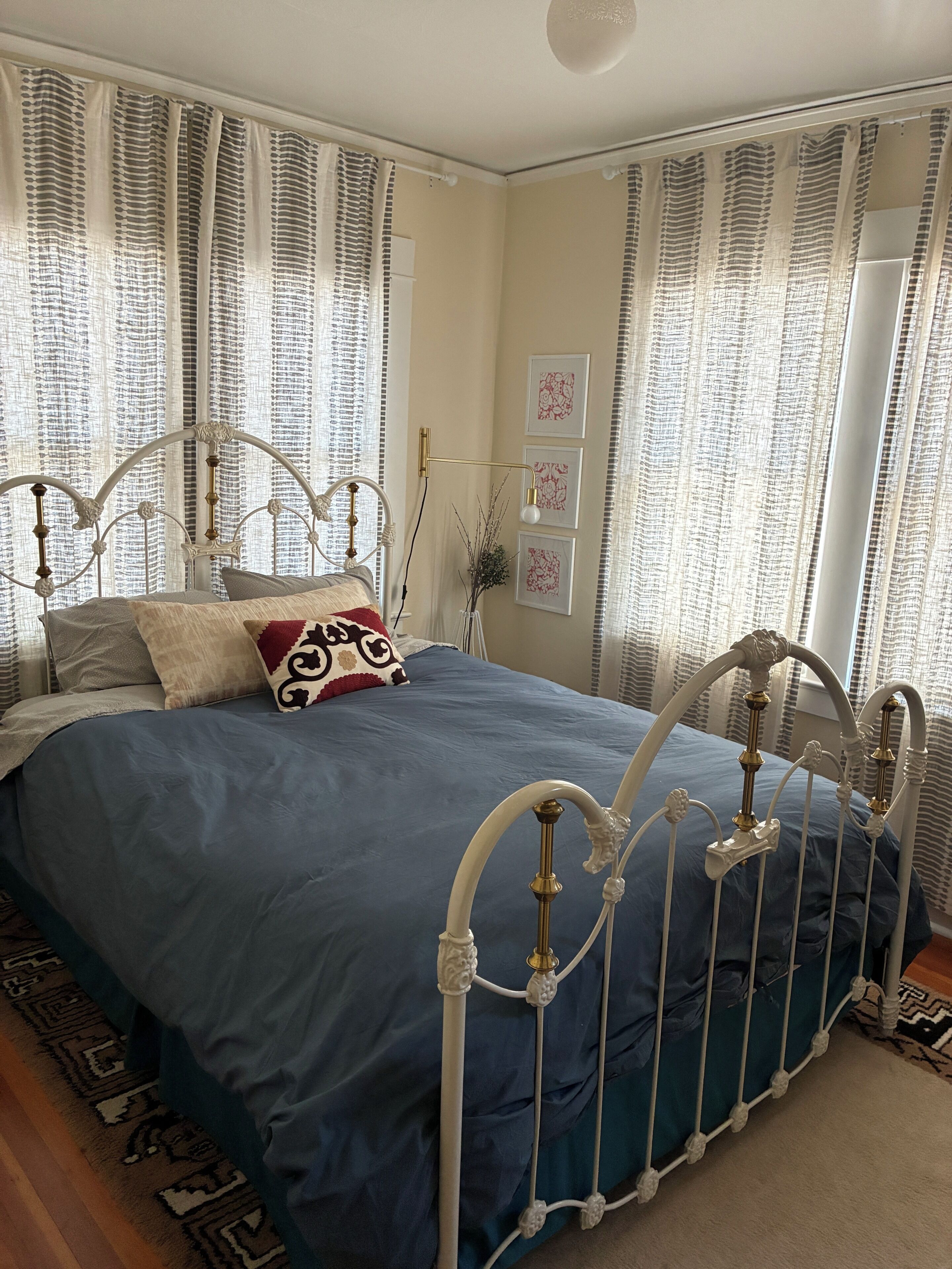 A bedroom with a metal bed frame, a blue bedspread, and patterned curtains.