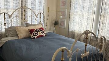 A bedroom with a metal bed frame, a blue bedspread, and patterned curtains.
