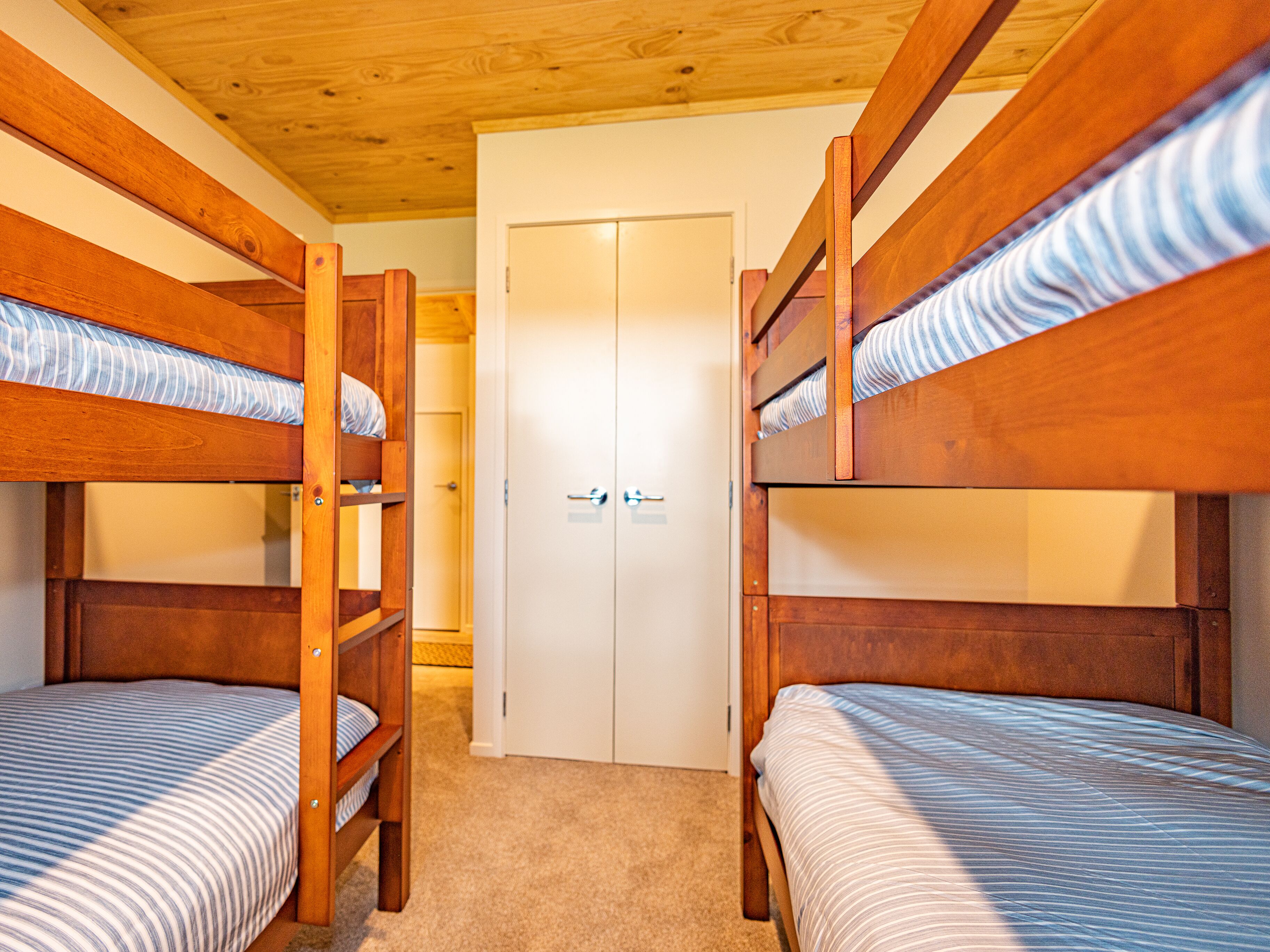 A room with two bunk beds, a white door, and wooden ceiling beams.