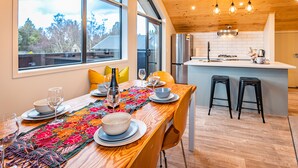 A modern kitchen with a wooden ceiling, large windows, and a dining area with a table set for two.