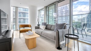A modern living room with a sofa, coffee table, and chairs, large windows with city views, and a flat-screen TV. - Bright Canary Wharf 1BR, steps to South Quay light rail, by Blueground (London)