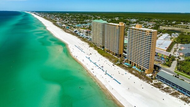 A beachfront hotel with multiple high-rise buildings, a sandy beach, and a clear blue ocean.