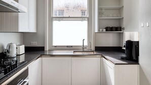 Une cuisine moderne avec des meubles blancs, un plan de travail noir, une fenêtre et une machine à café.