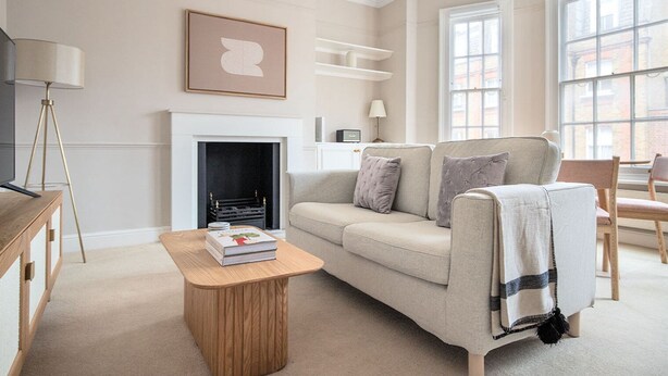 Un salon avec un canapé beige, une table basse en bois, une cheminée et une grande fenêtre.