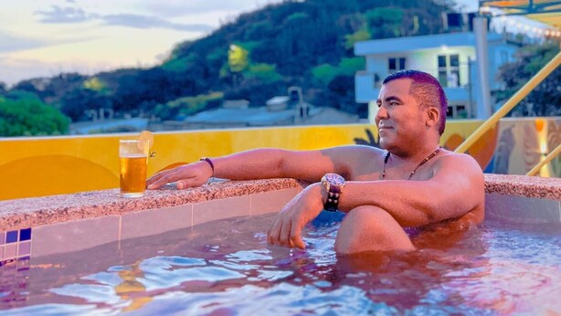 A person relaxing in a hot tub with a view of a hill and a building in the background. - Tropical Hostel Santa Marta (Santa Marta)