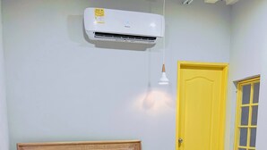 A neatly made bed with a wooden headboard, a small bedside table with a plant, and a yellow door with a window. - Tropical Hostel Santa Marta (Santa Marta)