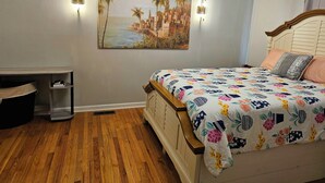 A bedroom with a wooden floor, a bed with a floral bedspread, a painting of a coastal scene, and two wall-mounted lights. - RockSide Suite: Stairs & Ramp Access • Masters Tournament • Lake Getaways (Appling)