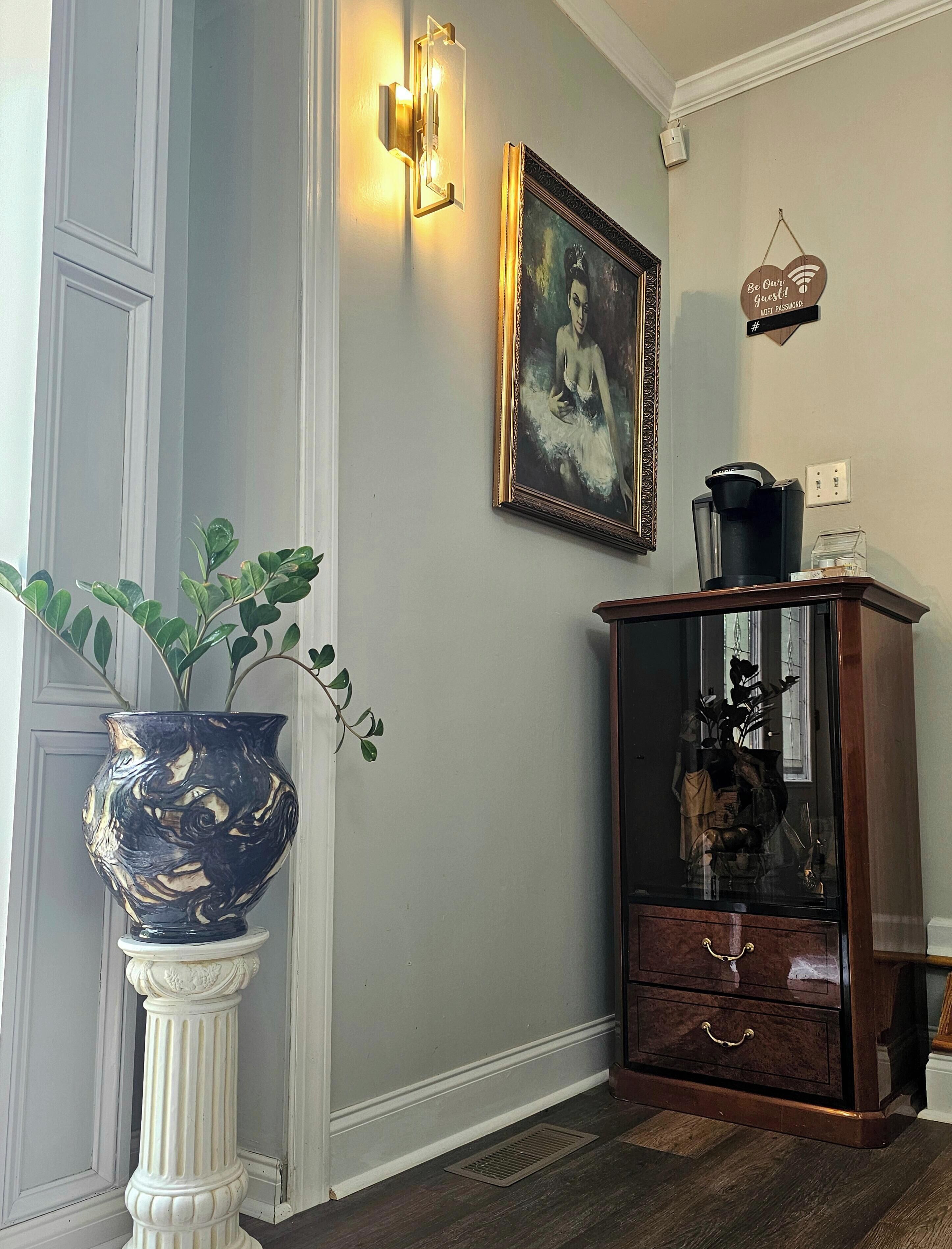 Une pièce comprenant un grand vase, un tableau encadré, un meuble avec un miroir et un luminaire fixé au mur.