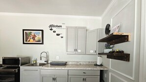 A kitchen with grey cabinets, a microwave, a sink, and a decorative wall sign. - RockSide Suite: Stairs & Ramp Access • Masters Tournament • Lake Getaways (Appling)