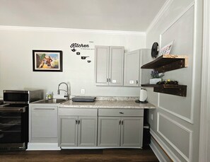 A kitchen with grey cabinets, a microwave, a sink, and a decorative wall sign.