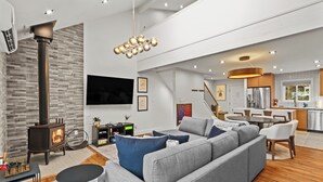 A modern living room with a large gray sectional sofa, a fireplace, and a dining area with a kitchen in the background. - Camelback - Game Room, Near Hiking & Waterparks (Tannersville)