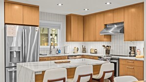 A modern kitchen with wooden cabinets, stainless steel appliances, and a marble island with bar stools. - Camelback - Game Room, Near Hiking & Waterparks (Tannersville)
